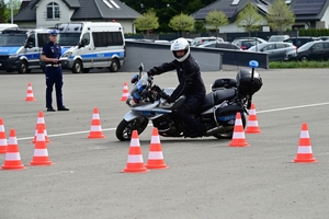 Policjanci na placu manewrowym - podczas konkurencji jazdy motocyklem. Policjant w kasku i na motocyklu jedzie po torze.