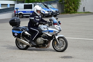 Policjanci na placu manewrowym - podczas konkurencji jazdy motocyklem. Policjant w kasku i na motocyklu jedzie po torze.