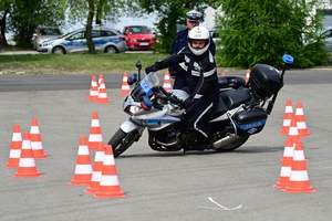 Policjanci na placu manewrowym - podczas konkurencji jazdy motocyklem. Policjant w kasku i na motocyklu jedzie po torze.