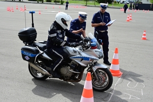 Policjanci na placu manewrowym - podczas konkurencji jazdy motocyklem. Policjant w kasku i na motocyklu jedzie po torze.
