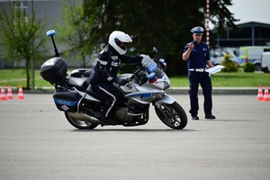 Policjanci na placu manewrowym - podczas konkurencji jazdy motocyklem. Policjant w kasku i na motocyklu jedzie po torze.