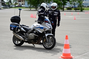 Policjanci na placu manewrowym - podczas konkurencji jazdy motocyklem. Policjant w kasku i na motocyklu jedzie po torze.