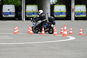 Policjanci na placu manewrowym - podczas konkurencji jazdy motocyklem. Policjant w kasku i na motocyklu jedzie po torze.