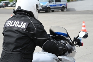 Policjanci na placu manewrowym - podczas konkurencji jazdy motocyklem. Policjant w kasku i na motocyklu jedzie po torze.