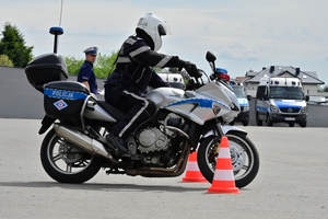 Policjanci na placu manewrowym - podczas konkurencji jazdy motocyklem. Policjant w kasku i na motocyklu jedzie po torze.