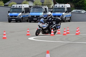 Policjanci na placu manewrowym - podczas konkurencji jazdy motocyklem. Policjant w kasku i na motocyklu jedzie po torze.