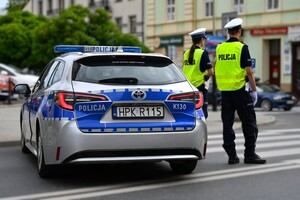 Policjant i policjantka oraz radiowóz stojący na drodze.