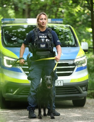 Policjantka stojąca ze swoim służbowym psem na tle radiowozu