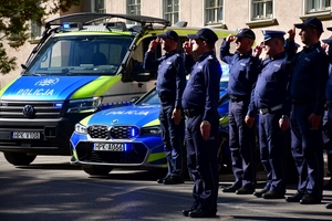Policjanci oddają honory zmarłemu Koledze - upamiętnienie pod budynkiem Komendy Wojewódzkiej Policji w Rzeszowie, po prawej i lewej stronie stoją policyjne radiowozy z włączonymi sygnałami świetlnymi i dźwiękowymi.