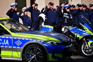 Policjanci oddają honory zmarłemu Koledze - upamiętnienie pod budynkiem Komendy Wojewódzkiej Policji w Rzeszowie, po prawej i lewej stronie stoją policyjne radiowozy z włączonymi sygnałami świetlnymi i dźwiękowymi.