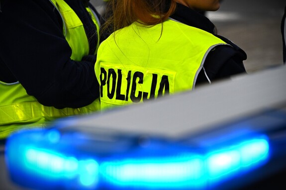 Belka policyjnego radiowozu, w tle dwoje policjantów