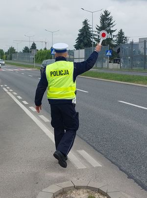 Na zdjęciu umundurowany policjant ruchu drogowego, w prawej, podniesionej do góry ręce trzyma tarczę do zatrzymywania pojazdów.