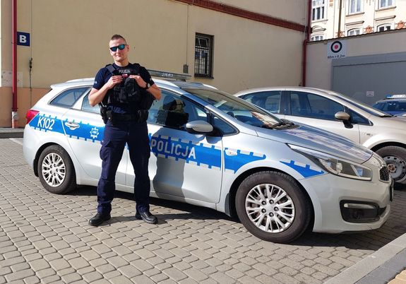 Na zdjęciu w mundurze, na tle policyjnego radiowozu stoi st. post. Tomasz Pipała.