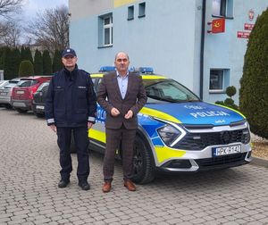 Na zdjęciu w policyjnym mundurze komisarz Tomasz Bajda Komendant Komisariatu Policji w Tyczynie z  Wójtem Gminy Hyzne Bartłomiejem Kuchta, obok nich policyjny radiowóz.