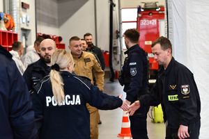 Na zdjęciu umundurowaniu policjanci oraz strażacy w tle wozy strażackie.