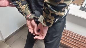 Na zdjęciu mężczyzna ubrany w kurtkę do pasa i czarnee spodnie, na rękach trzymanych z tyłu ma założone kajdanki.