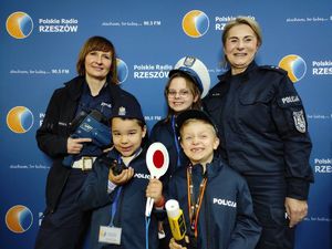 Na zdjęciu na ściance Pol siego Radia Rzeszów stoją dwie umundurowane policjantki, obok nich dzieci w policyjnych mundurkach.