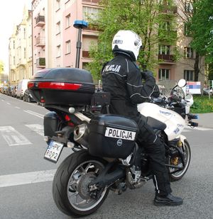 Na zdjęciu siedzący na służbowym motocyklu funkcjonariusz ruchu drogowego w pełnym umundurowaniu.