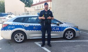 Na zdjęciu rzeszowski policjant, st. post. Marcin Popek w pełnym umundurowaniu przy policyjnym radiowozie.