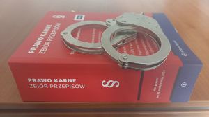 Na zdjeciu kodeks karny, na którym leża policyjne kajdanki.