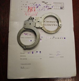 Na zdjęciu obwoluta na policyjne akta, na nich leżą kajdanki.