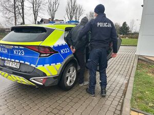 Na zdjeciu umundurowany policjant i mężczyzna w cywilnym ubraniu, który wsiada do radiowozu.