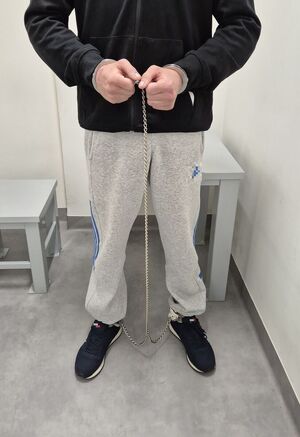 Na zdjeciu mężczyzna który na ręce i nogi na założone kajdanki zespolone.