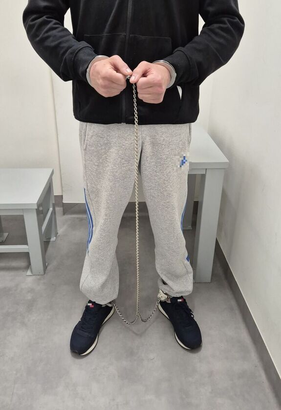 Na zdjeciu mężczyzna który na ręce i nogi na założone kajdanki zespolone.