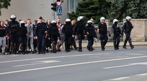Na zdjęciu umundurowani policjanci, za mini kibice.