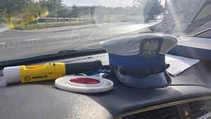 Na zdjeciu na podszybiu leży policyjna czapka ruchu drogowego, tarcza do zatrzymywania pojazdów i urządzenie do kontroli stanu trzeźwości.
