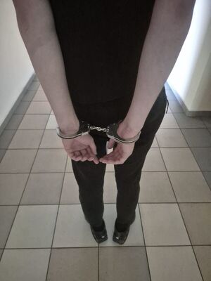 Na zdjęciu  stojący tyłem, ubrany na czarno mężczyzna, który na rękach ma założone kajdanki.