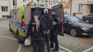 Zdjęcie przedstawia funkcjonariuszy prowadzących zatrzymanego