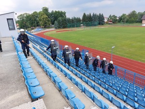 Policjanci tworzą tyralierę idą trybunami, które znajdują się na trybunach stadionu miejskiego w Ropczycach