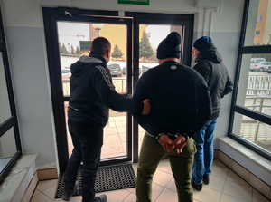 nieumundurowani policjanci wyprowadzający zatrzymanego mężczyznę z budynku komendy