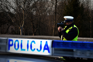 policjant ruchu drogowego dokonujący pomiaru prędkości, na pierwszym planie baner POLICJA