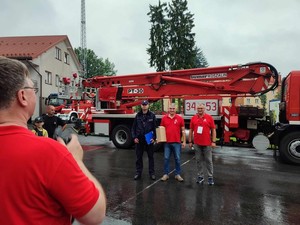 Policjant z organizatorami wydarzenia. W tle pojazd strażacki