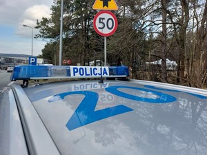 na pierwszym planie policyjny radiowóz, w tle znak ograniczenia prędkości do 50 km/h