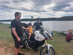 dziecko siedzące na motocyklu policyjnym, obok stoi mężczyzna i policjant