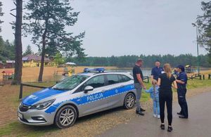 Policyjny radiowóz obok którego stoją ludzie i policjanci