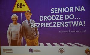 Plakat promujący akcję &quot;Senior na drodze do...bezpieczeństwa&quot;. Grafika przedstawia seniorów nad którymi widnieje znak drogowy.