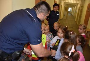 Dzieci w pomieszczeniu dla osób zatrzymanych. Policjant prezentuje maluchom wykrywacz metalu