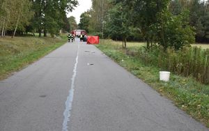 Miejsce wypadku drogowego. Droga na której widoczny jest po prawej stronie parawan z napisem Policja, w tle radiowóz i wóz strażacki