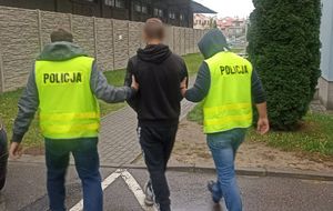 Policjanci w kamizelkach z napisem Policja prowadzą zatrzymanego mężczyznę