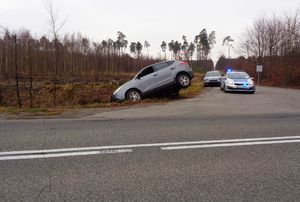 W przydrożnym rowie znajduje się samochód, którego tylna część wystaje na jezdnię. W tle radiowóz
