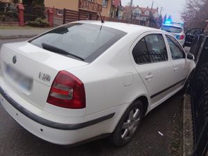 Samochód wjechał w ogrodzenie posesji. W tle radiowóz.