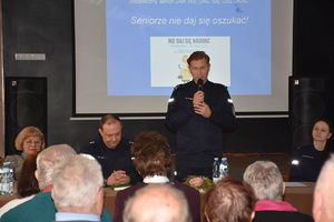 Policjant mówi przez mikrofon. W tle wyświetlona jest prezentacja.