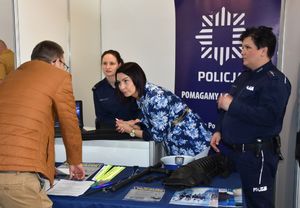 Policjantki na stoisku promującym pracę w Policji. Przy stoliku znajduje się mężczyzna.
