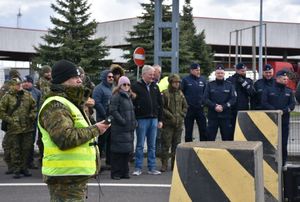 Funkcjonariusz Straży Granicznej. W tle na chodniku mundurowi i osoby cywilne