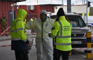 Człowiek w kombinezonie. Przy niem dwie osoby w kamizelkach dokonują jego kontroli