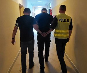 Policjanci prowadzą korytarzem zatrzymanego mężczyznę